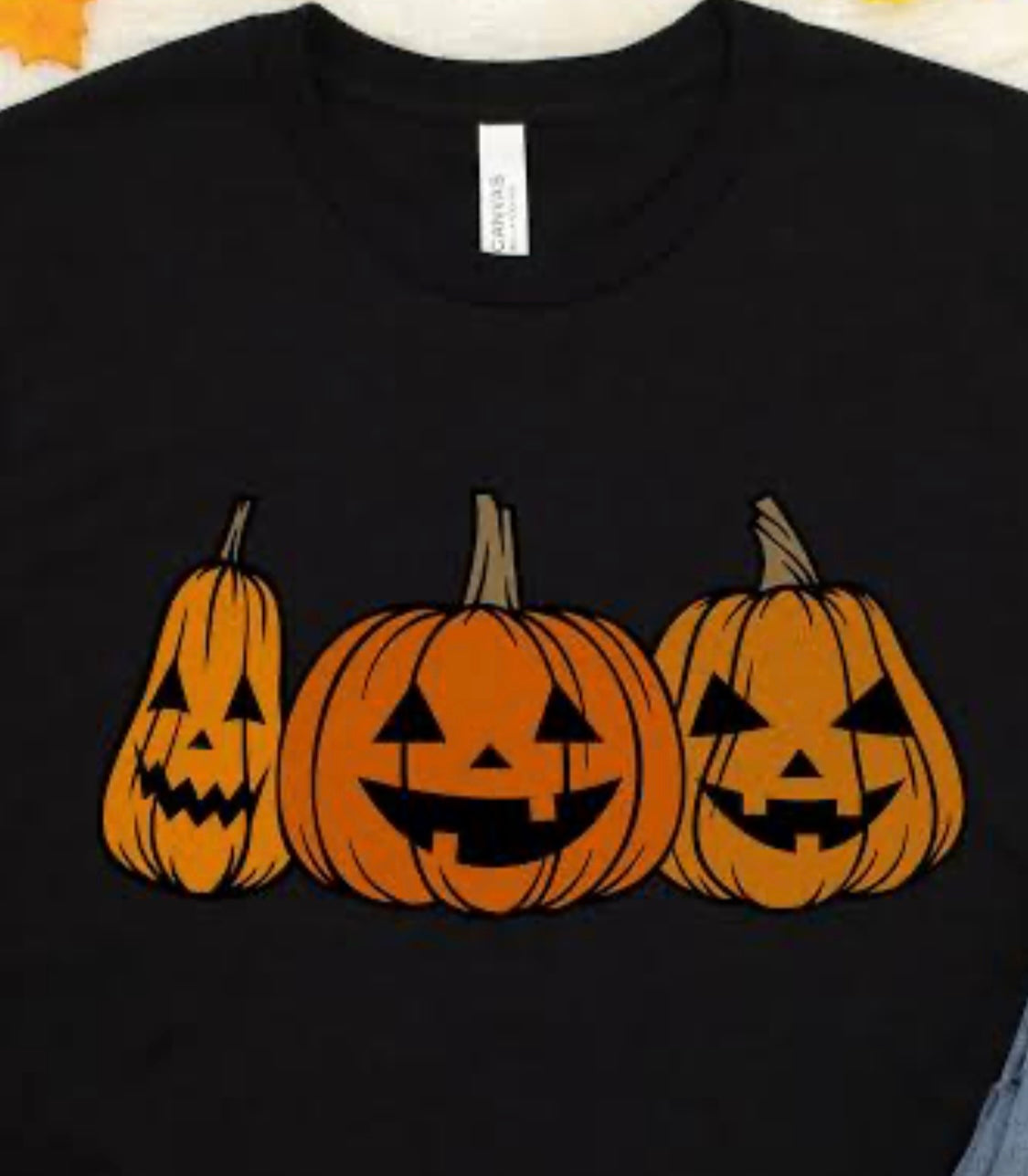 Black t-shirt with three jack-o'-lanterns printed on it.